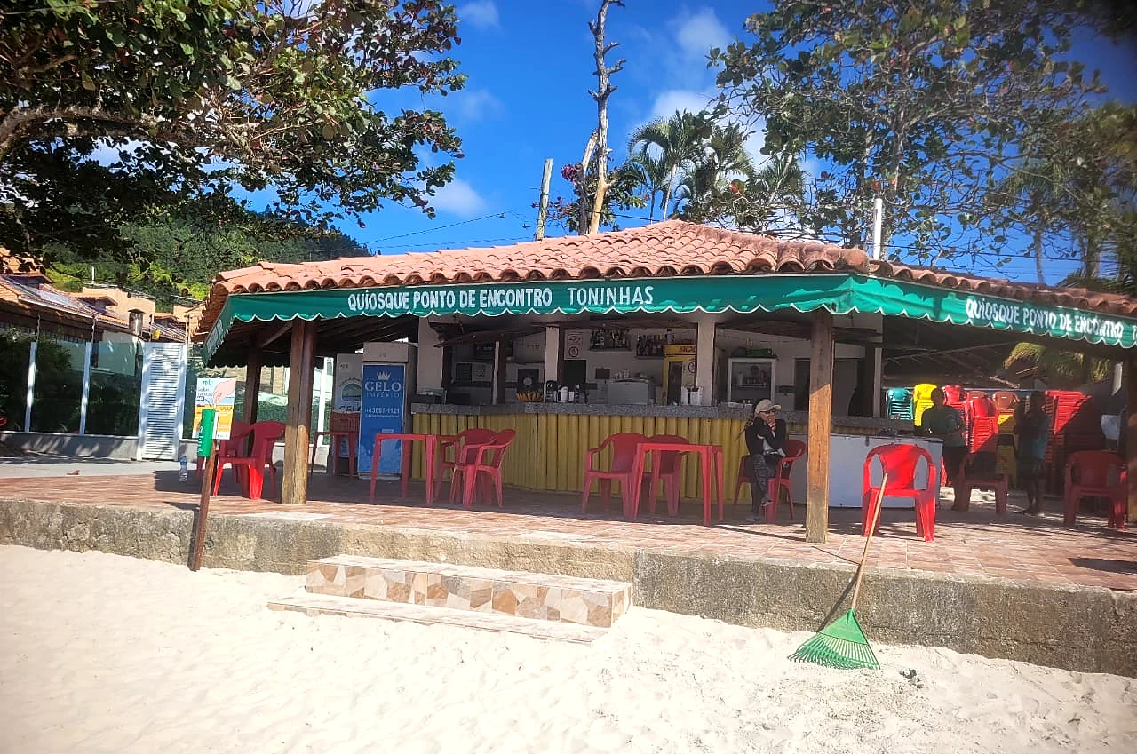 Quiosque visto da areia, com mesas e o morro ao fundo
