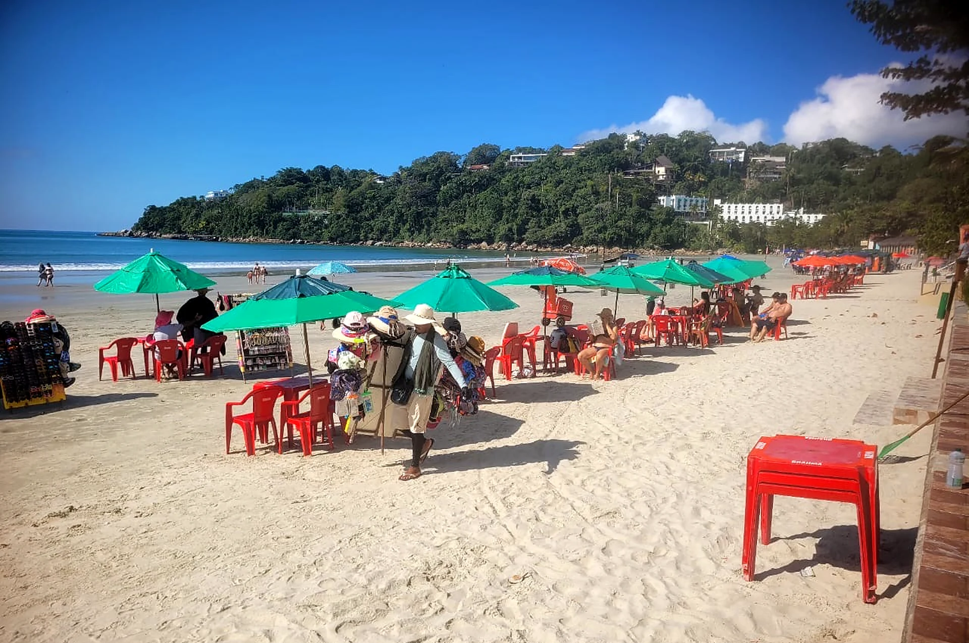 Faixa de areia da Praia das Toninhas com guarda-sóis verdes